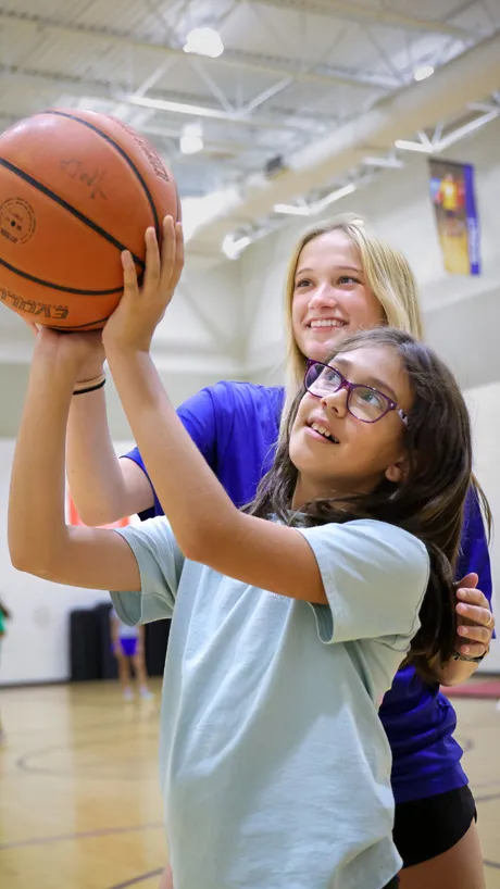 Camp counselor helping a child shoot basketballs