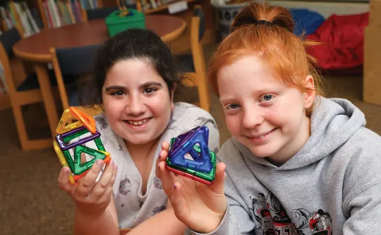 two girls hold magnetic tiles at a before school program