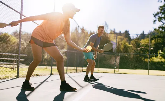 Man and woman playing doubles pickleball outside