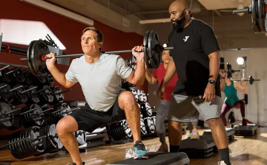 an instructor spots a member lifting a barbell