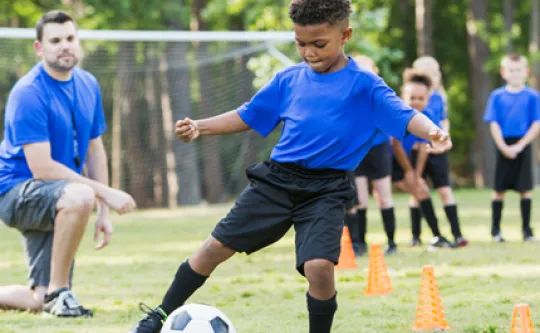 Coach watching a soccer player move through a kicking drill