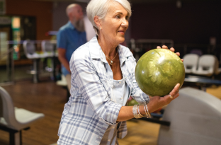 close up shot of woman with green bowling ball in stance about to take a turn rolling