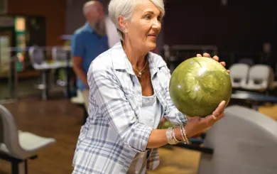 close up shot of woman with green bowling ball in stance about to take a turn rolling