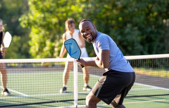 a man laughing as he plays pickleball