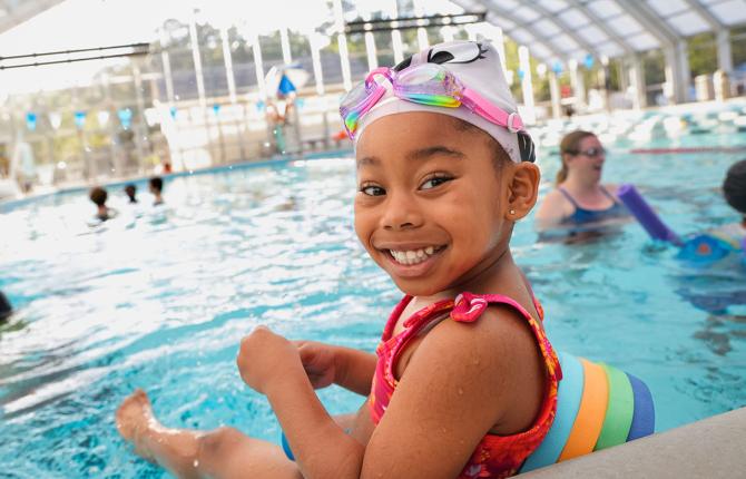 A preschooler with goggles and floties eagerly waits her turn for swim lessons